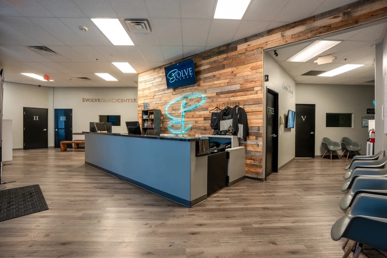 Evolve Dance Center lobby — reclaimed wood accent wall, neon teal E logo, and reception desk
